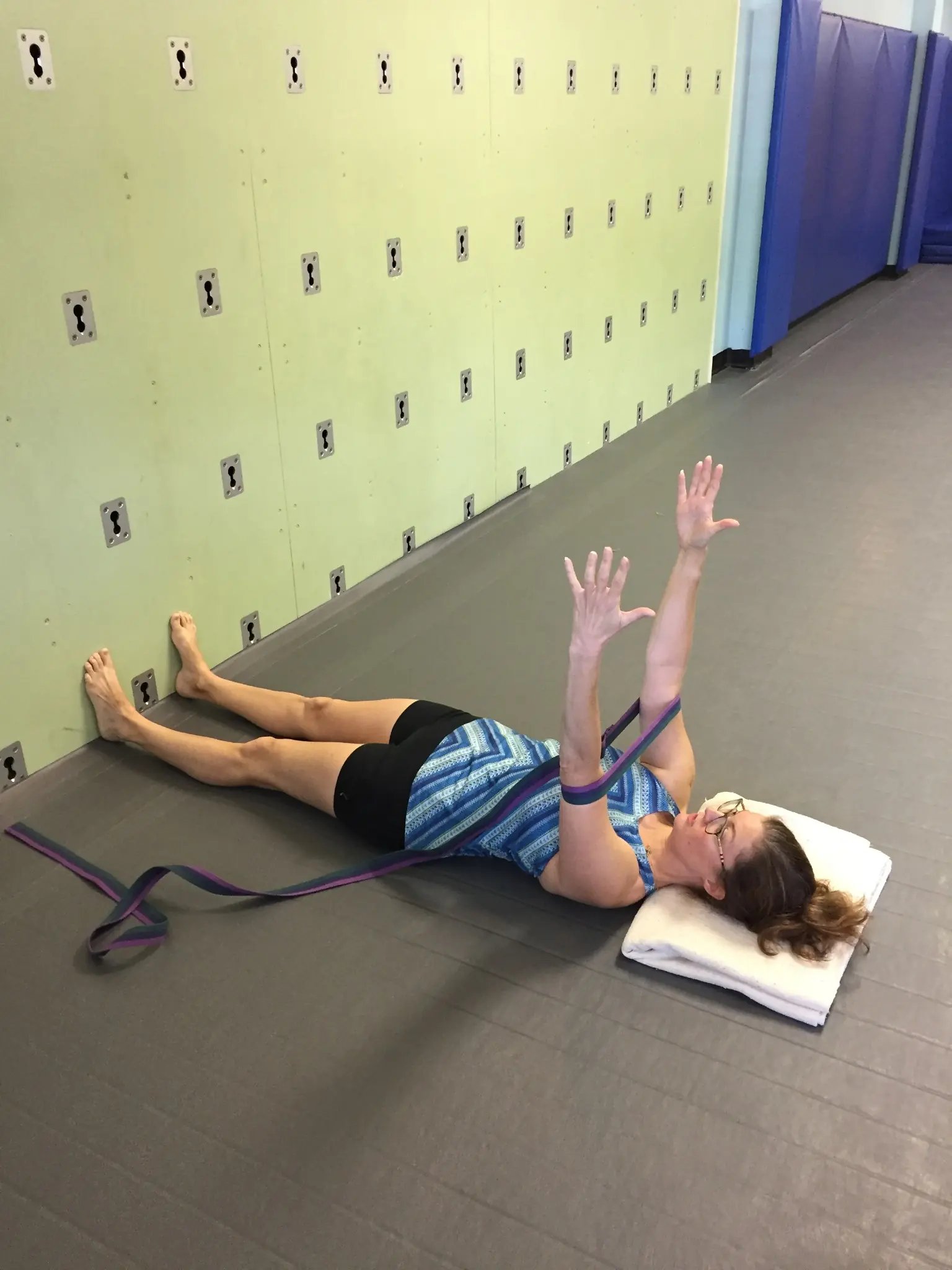A strap-supported reclining stretch with the feet at the wall